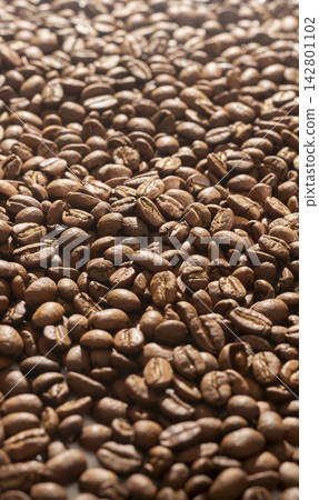 A close up angled shot of roasted coffee beans reveals the detailed surface of each bean. The macro perspective captures the warm brown tones and natural texture at a shallow depth A close up angled shot of roasted coffee beans reveals the detailed surface of each bean. The macro perspective captures the warm brown tones and natural texture at a shallow depth 142801102