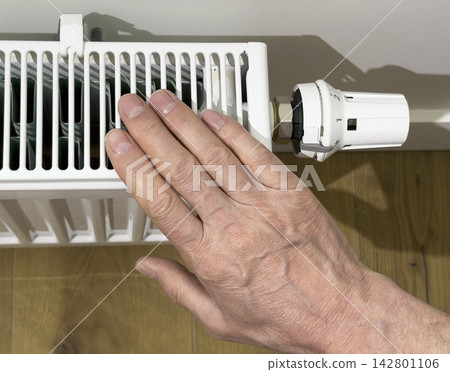 Hand adjusting a radiator thermostatic valve in a home interior. Heating control for temperature regulation and energy saving. Indoor maintenance concept for winter comfort.. Hand adjusting a radiator thermostatic valve in a home interior. Heating control for temperature regulation and energy saving. Indoor maintenance concept for winter comfort.. 142801106