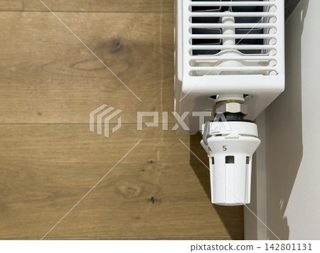 Thermostatic radiator valve on a white heater. Close up of heating control in a home interior. Energy saving temperature regulation for indoor comfort.. Thermostatic radiator valve on a white heater. Close up of heating control in a home interior. Energy saving temperature regulation for indoor comfort.. 142801131