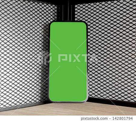 Phone mockup with a bright green chroma key screen stands upright in a black wire mesh shelving Phone mockup with a bright green chroma key screen stands upright in a black wire mesh shelving 142801794