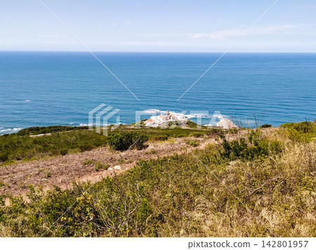 This scenic coastal vista features a solitary lighthouse perched on a rugged grassy cliff overlooking the deep blue sea. The nobody landscape evokes feelings of freedom and peace. 142801957