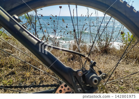 Framed by a bicycle wheel, a peaceful coastal view of the blue sea evokes feelings of freedom, active adventure, and serene summer exploration on a sunny day. There are no people. Framed by a bicycle wheel, a peaceful coastal view of the blue sea evokes feelings of freedom, active adventure, and serene summer exploration on a sunny day. There are no people. 142801975