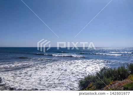 A serene, vast blue ocean with rolling white waves crashing near a sunny coastal shoreline under a bright, clear sky. This peaceful nature scene evokes tranquility. Nobody. A serene, vast blue ocean with rolling white waves crashing near a sunny coastal shoreline under a bright, clear sky. This peaceful nature scene evokes tranquility. Nobody. 142801977