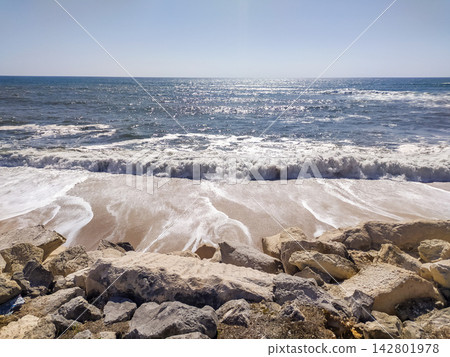 A breathtaking sunny view of a wild rocky beach where powerful ocean waves crash on the shore, evoking a sense of calm and freedom. Ideal for travel and wellness projects. Nobody. A breathtaking sunny view of a wild rocky beach where powerful ocean waves crash on the shore, evoking a sense of calm and freedom. Ideal for travel and wellness projects. Nobody. 142801978
