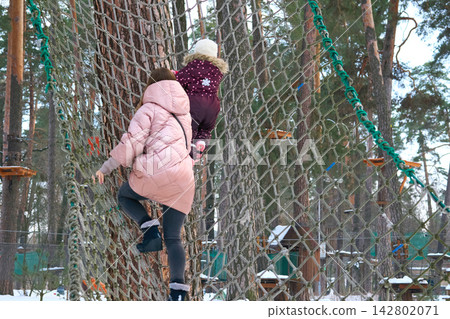 Mother with daughter playing on winter gladiator rope net Mother with daughter playing on winter gladiator rope net 142802071