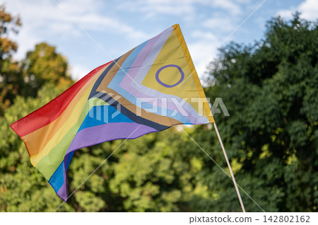 Rainbow Pride Flag with Intersex Symbol Against Blue Sky Rainbow Pride Flag with Intersex Symbol Against Blue Sky 142802162