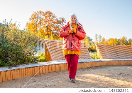 woman hiking in autumn park. lady enjoying warm drink in nature. Body positive concept, outdoor activity and healthy lifestyle in vibrant fall season landscape. 142802251