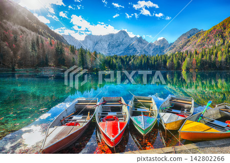 Unforgatable view of Fusine lake with boats and Mangart peak on background. Unforgatable view of Fusine lake with boats and Mangart peak on background. 142802266