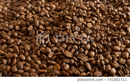 A horizontal frame of roasted coffee beans is filled with warm golden brown tones throughout. The slightly varied depth and lighting gives the surface a lively dimensional quality. A horizontal frame of roasted coffee beans is filled with warm golden brown tones throughout. The slightly varied depth and lighting gives the surface a lively dimensional quality. 142802311