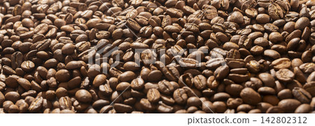 A shallow focus shot of roasted coffee beans shows a soft blurred foreground and sharp middle detail. The warm brown beans fade gently at the edges creating a dreamy texture. A shallow focus shot of roasted coffee beans shows a soft blurred foreground and sharp middle detail. The warm brown beans fade gently at the edges creating a dreamy texture. 142802312