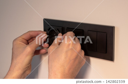 Electrical socket installation in modern apartment wall box. Hands of repairman mounting black power Electrical socket installation in modern apartment wall box. Hands of repairman mounting black power 142802339