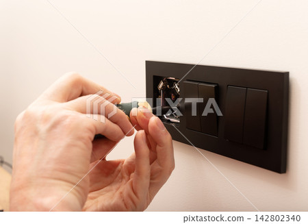 Electrician installing power outlet box using hand screwdriver tool. Repairman tightening black Electrician installing power outlet box using hand screwdriver tool. Repairman tightening black 142802340