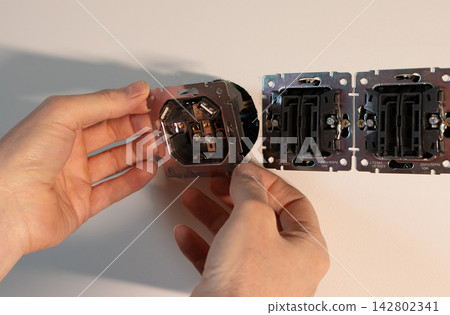 Electrician installing power outlet mechanism into wall socket box. Hands placing metal fixture unit Electrician installing power outlet mechanism into wall socket box. Hands placing metal fixture unit 142802341