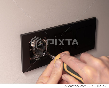 Electrician installing power outlet on wall using hand screwdriver tool. Repairman tightening black Electrician installing power outlet on wall using hand screwdriver tool. Repairman tightening black 142802342