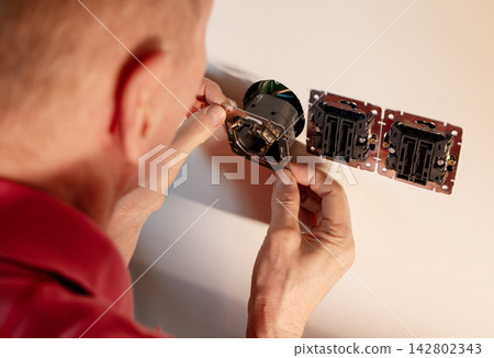 Electrician installing power socket box mechanism in wall panel. Senior repairman fixing electrical Electrician installing power socket box mechanism in wall panel. Senior repairman fixing electrical 142802343