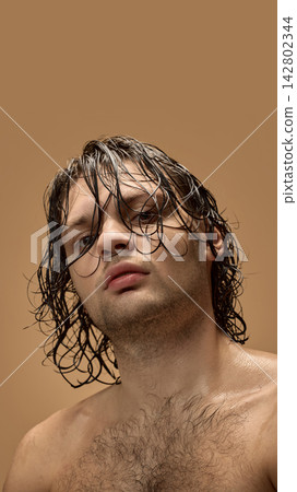 Long haired man looking forward with wet strands across face 142802344