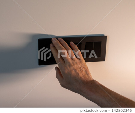 Electrician pressing black power light switch frame on white wall. Hand of repairman testing triple Electrician pressing black power light switch frame on white wall. Hand of repairman testing triple 142802346
