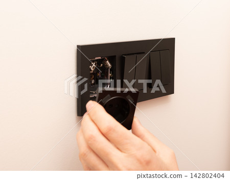 Power socket outlet frame mounting on electric wall box. Hands of electrician attaching black cover Power socket outlet frame mounting on electric wall box. Hands of electrician attaching black cover 142802404