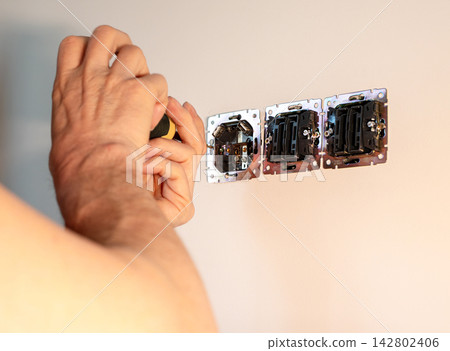 Power socket outlet installation on residential room wall box. Technician hands screwing metal Power socket outlet installation on residential room wall box. Technician hands screwing metal 142802406