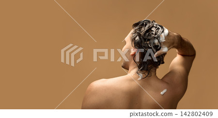 Young man washing foamy hair against brown studio background 142802409