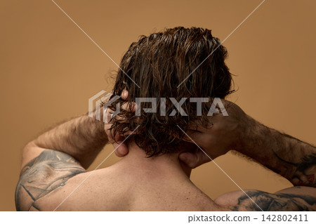 Man massaging long wet hair against warm brown background Man massaging long wet hair against warm brown background 142802411