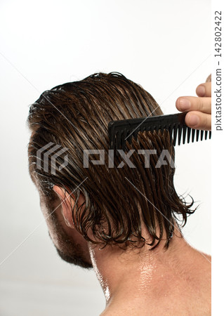 Man combing long wet hair down the back of his head Man combing long wet hair down the back of his head 142802422
