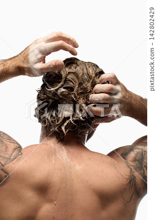 Tattooed man massaging shampoo into wet hair with both hands Tattooed man massaging shampoo into wet hair with both hands 142802429