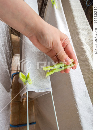 Hand putting green plastic clothespin on white towel drying on a clothesline Hand putting green plastic clothespin on white towel drying on a clothesline 142802504