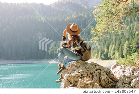 Young woman traveler enjoys fresh air and a beautiful view of the lake and mountains. Active life 142802547