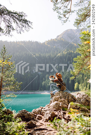 Young traveler is resting and taking pictures of amazing landscape with mountains and lake. Blogging Young traveler is resting and taking pictures of amazing landscape with mountains and lake. Blogging 142802549