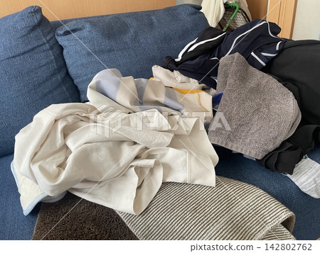 A pile of laundry, including clothes and towels, scattered on the sofa. A pile of laundry, including clothes and towels, scattered on the sofa. 142802762