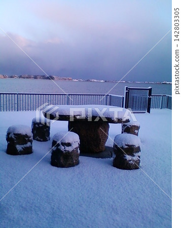 A stone bench buried in the accumulating snow and the tranquil lakeside. A stone bench buried in the accumulating snow and the tranquil lakeside. 142803305