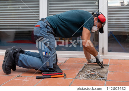 Worker kneeling with mask carefully repairing damaged tile floor indoors Worker kneeling with mask carefully repairing damaged tile floor indoors 142803682
