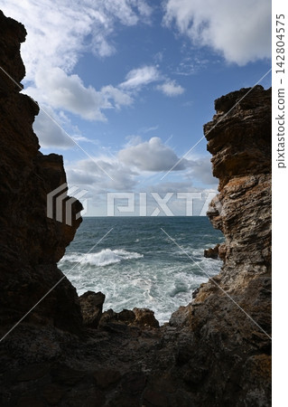 [Aomori] A view of the blue sky and the crashing sea seen through a gap in the rocks. 142804575