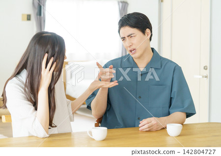 一對年輕的日本夫婦在客廳裡爭吵,互相指責。 一對年輕的日本夫婦在客廳裡爭吵,互相指責。 142804727