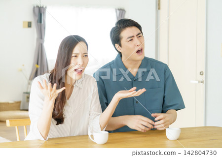 一對年輕的日本夫婦在客廳裡爭吵,兩人雙臂張開。 一對年輕的日本夫婦在客廳裡爭吵,兩人雙臂張開。 142804730