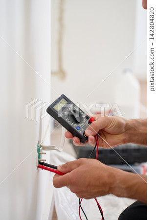 Electrician testing wall socket voltage with digital multimeter Electrician testing wall socket voltage with digital multimeter 142804820