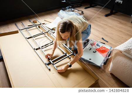 Woman assembling shelving frame on floor at home Woman assembling shelving frame on floor at home 142804828