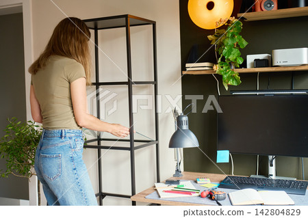 Woman placing glass shelf into shelving unit beside home office desk Woman placing glass shelf into shelving unit beside home office desk 142804829