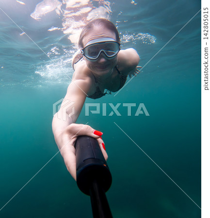Clear ocean selfie captured by young woman wearing swimming goggles while diving underwater Clear ocean selfie captured by young woman wearing swimming goggles while diving underwater 142805015