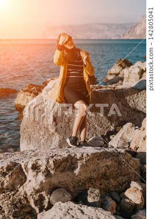 Woman Coast Sunset Young woman in yellow jacket sitting on rocky seashore enjoying warm sunlight during autumn vacation trip 142805041