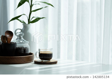 Coffee glass cup and roasted coffee beans in a glass jar on a white table Coffee glass cup and roasted coffee beans in a glass jar on a white table 142805134