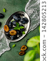 Fresh Ripe Plums with Green Basil Leaves on a Metal Plate	 142805213