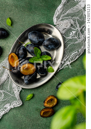 Fresh Ripe Plums with Green Basil Leaves on a Metal Plate Fresh Ripe Plums with Green Basil Leaves on a Metal Plate 142805213