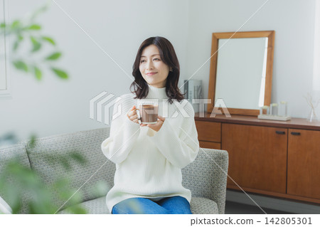 Middle-aged woman drinking coffee in the living room Middle-aged woman drinking coffee in the living room 142805301
