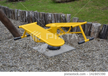 Yellow outdoor sports equipment designed for physical training and waist turning exercises, placed on a gravel ground in an outdoor street gym or park area. Yellow outdoor sports equipment designed for physical training and waist turning exercises, placed on a gravel ground in an outdoor street gym or park area. 142805390