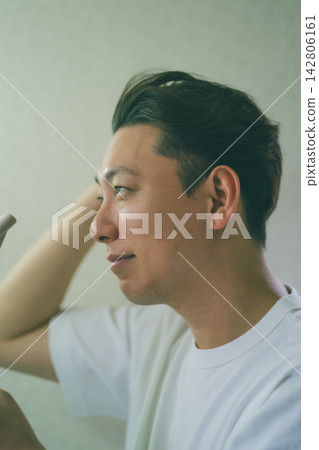 A profile view of a man in his 40s styling his hair with a hairdryer and his fingers. A profile view of a man in his 40s styling his hair with a hairdryer and his fingers. 142806161