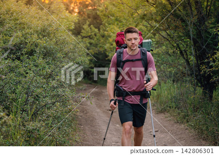 Handsome man trekking through woods path with backpack and poles Handsome man trekking through woods path with backpack and poles 142806301