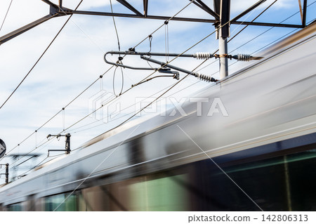 A low-angle shot capturing the exhilarating speed of a train speeding under overhead power lines. A low-angle shot capturing the exhilarating speed of a train speeding under overhead power lines. 142806313