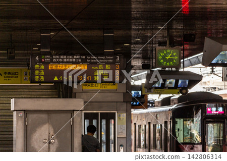 A low-angle view of a conventional train station platform, showing an electronic display board, departure board, and clock. A low-angle view of a conventional train station platform, showing an electronic display board, departure board, and clock. 142806314